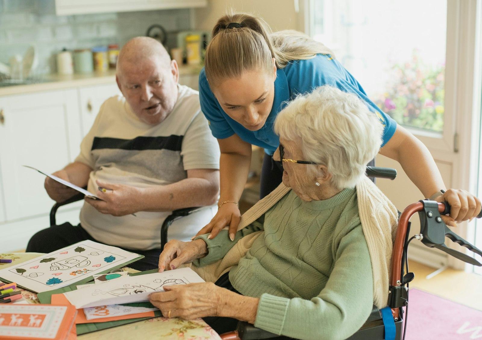 A caregiver helping an elderly couple at their kitchen table